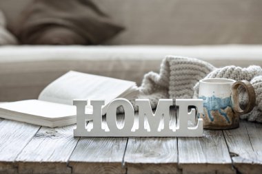 Dekoratif ev, çay, örgü ögesi ve odanın iç kısmının bulanık arkaplanı üzerine kitap içeren ev kompozisyonu.