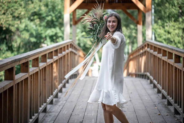 木製の橋の上にエキゾチックな花の花束と白いドレスの美しい女の子 — ストック写真