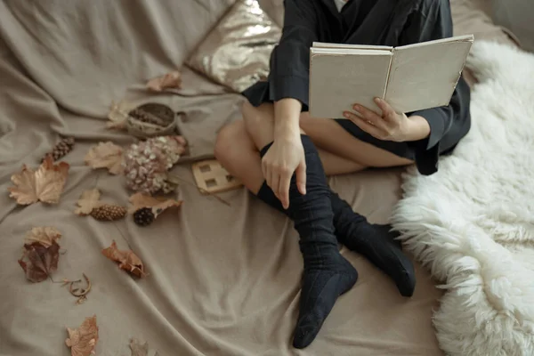 一个穿着保暖长袜的女孩躺在床上看书 那是一个舒适的秋天的背景 — 图库照片