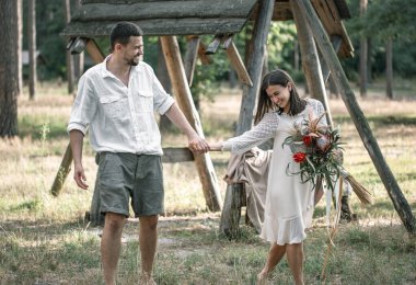 Genç adam ve kadın şık giyinmiş, bir buket egzotik çiçekle ormanda yürüyorlar, doğada bir randevuda..