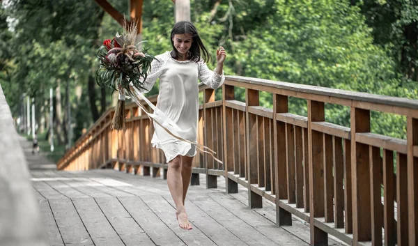 木製の橋の上にエキゾチックな花の花束と白いドレスの美しい女の子 — ストック写真