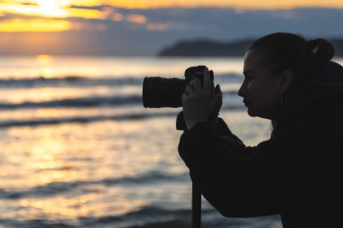 Sahilde altın saat boyunca kameralı bir kadın, özgürlük, ruh hali ve yaratıcı enerjiyi yansıtıyor..