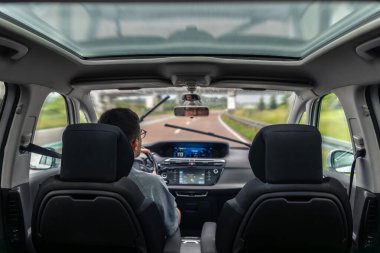 Yağmurdan sonra yağmurlu bir yolda, içeriden yakalanmış bir adam araba kullanıyor. Panoramik çatı ve yumuşak ışık sakinlik, odak ve günlük hareketlerin karışımını yaratır..