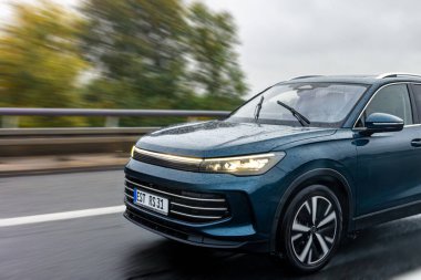 Parlak mavi bir SUV yağmurda ıslak bir otoyolda hızla sürer. Parlayan farlar ve su yansımaları güçlü bir hareket ve özgürlük hissi yaratır..