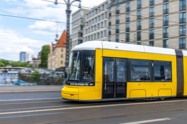 Sarı bir tramvay, hızlı, sürdürülebilir ve rahat şehir ulaşımını sembolize eden yüksek binalarla modern şehir sokaklarında hızla ilerliyor..
