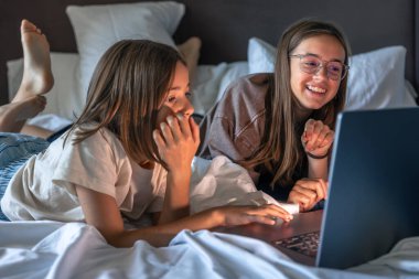 Yastıklar ve battaniye, kızlar içeriğe tepki verirken bir ev sahnesi hazırlıyor. Şaşırtma ve kahkaha karışımı, hafif bir titreşim ve kolay bir yakınlık..