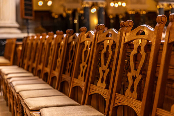 A sequence of carved wooden chairs with padded seats in golden light. Shallow depth of field emphasizes ornament and the calm atmosphere of the hall.