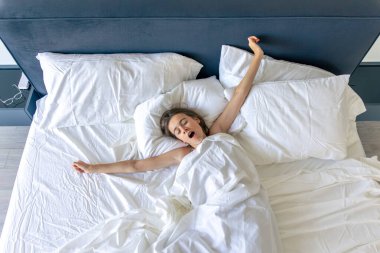 Genç bir kız gün ışığında esneyip, bembeyaz yatak örtüleri üzerinde gerinir. Rahat bir hayat ve güne nazik bir başlangıç..