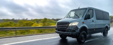 Yağmurda ıslak bir otoyol boyunca giden modern gri bir minibüs güvenilirliği, teknolojiyi ve modern lojistiğin hızını temsil ediyor..