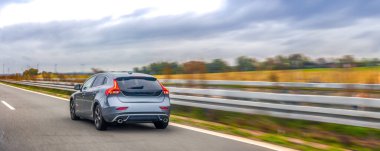 Bulutlu gökyüzünün altında hızla giden modern gri araba özgürlüğü, enerjiyi ve modern hareketliliğin rahatlığını simgeliyor..