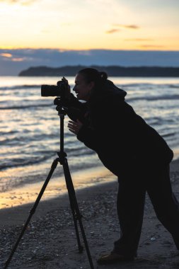 Gün batımında deniz kenarında tam yükseklikte genç bir kadının dikey görüntüsü. Sıcak su yansımaları ve çekim sürecine odaklan.