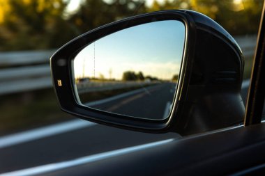 Yan ayna günbatımında otoyolu gösteriyor. Arkadaki yolu ve günlük yolculuk havasını simgeliyor. Özgürlüğün, seyahatin ve yansımanın bir karışımı..