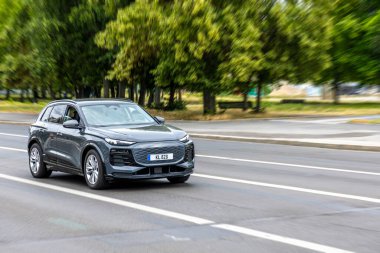 Bulanık yeşil bir arka plan hareketi ve günlük hareketliliği vurgularken, modern gri bir SUV şehir caddesi boyunca sürüyor..