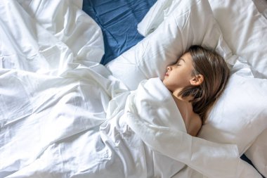 Genç bir kız, çarşafa sarılı olarak huzur içinde uyuyor, yukarıda yakalanmış. Sakin güvenlik, rüya gibi ruh hali ve rahat ev istirahatı..