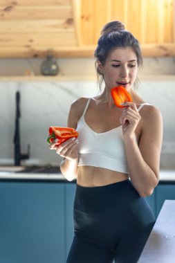 Zarif bir kadın diğer yarısını tutarken dudaklarına bir dilim kırmızı biber getirir. Parlak ışık ve asgari ayar sağlığın ve dikkatli beslenmenin göstergesi..