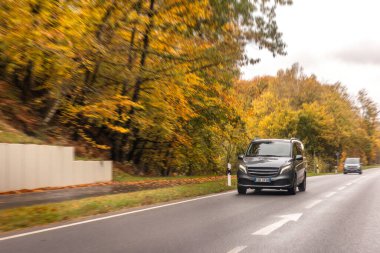 Karanlık bir minivan, sonbahar tepeleri ve ormanın yanında düz bir otoyol boyunca ilerliyor, uzayı, güvenliği ve seyahat rahatlığını taşıyor..