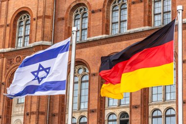 Alman ve İsrail bayrakları, uluslar arasındaki dostluğu, diplomasiyi ve birliği simgeleyen tarihi tuğla bir binanın yanında yan yana sallanıyor..
