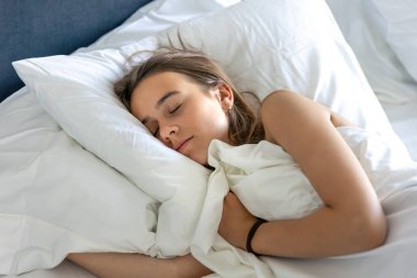 Yataktaki kız başparmağını kaldırır ve şakacı bir şekilde gülümser. Destekleyici ruh hali mizahı ev rahatlığı ve gençlik havası.