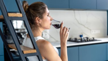 Modern bir mutfakta merdivenlerde oturmuş, sakince şarap yudumlayan bir kadının yan görüntüsü. Temiz çizgiler ve gün ışığı rahatlama ve rahatlama iletir..