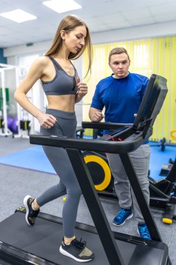 Bir kadın hasta rehabilitasyon merkezinde koşu bandında koşarken, bir doktor hızını ve şeklini izliyor. Aktif iyileşme ve dayanıklılığın yeniden inşası için parlaklık ayarları.