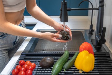 Yakın plan, lavabonun üzerinde akan suyun altında bir kadının avokadoyu duruladığını gösteriyor. Sağlıklı bir menü için malzeme hijyeni ve tazeliği üzerinde duruluyor..