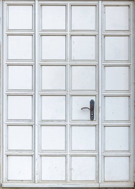 Beyaz kapının önü, karanlık tarafı olan kare panellerden oluşan ritmik bir ızgarayla kaplı. Nötr renk ve ince yaş işaretleri minimalist kentsel hissi vurguluyor.