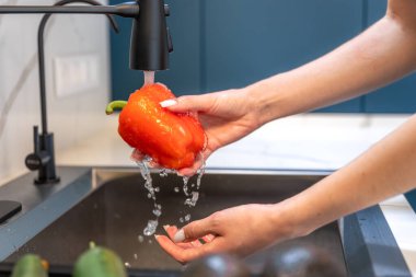 Yakından bakınca lavabonun üstünde kırmızı dolmalık biber çalan bir kadın görülüyor. Temiz damlalar ve temiz bir iç mekan hijyen ve sağlıklı yemek hazırlığını vurgular..