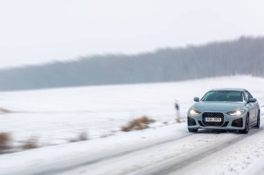 Farları olan bir araba, kar tanelerinin hız ve enerjiyi vurguladığı beyaz bir araziyi kesiyor. Editör içeriği, görünür plaka.