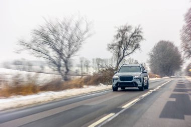 Güçlü hareket bulanıklığı ve parlak bir gökyüzü yollarda özgürlük hissi veriyor. Kenarlarda kar ve temiz asfalt hareketlilik, lojistik ve kış karayolu güvenliği temaları.