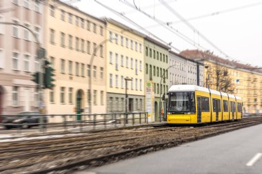 Parlak tramvay, sıcak binalar ve hız bulanıklığıyla sokak raylarında hareket halindeyken yakalandı. Yumuşak kış ışığı, akıllı şehir hareketliliğini, sürdürülebilir toplu taşıma ve kentsel yaşam tarzı kavramlarını destekler.