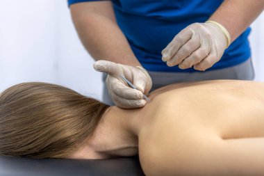 Muayene sırasında eldivenli bir doktor omuz ve köprücük kemiği bölgesini incelerken kadın hasta hislerine odaklanıyor. Nötr klinik içi ağrı kesici ve iyileşme konusunda tıbbi içeriğe uygun.