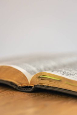 Omurganın yakın çekimi ve yumuşak ışık ve altın kenarlı ahşap bir masanın üzerinde açık bir İncil 'in sayfaları. Sahne, yavaş yaşam rutinini, çalışmayı ve huzurlu bir şekilde kutsal kitaba gömülmeyi öneriyor..