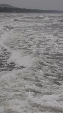 Dikey dron çekimi, karamsar atmosferde okyanus dalgalarının kıyı şeridinde hareket ettiğini ve kırıldığını gösteriyor. Sinematik hava görüntüsü, özgürlük ve doğa kavramı için dramatik bir seyahat ve açık hava arka planı yaratır..