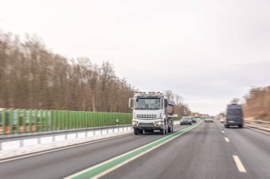 Large dump truck driving on multilane road with snow and forest background. Dynamic motion highlights industrial business and transportation infrastructure concepts.