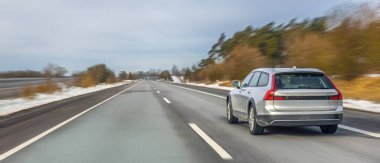 Modern steyşın araba, orman ve karlı kırsal bölgelerde hareket bulanıklığı ile çevrili bir kış otoyolu boyunca sürüyor. Yol yolculuğu, hareketlilik ve modern ulaşım kavramı.