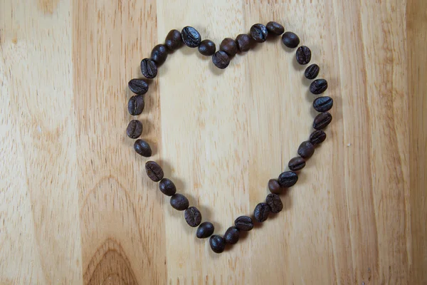 Los granos de café hacen en forma de corazón sobre fondo de madera —  Fotos de Stock