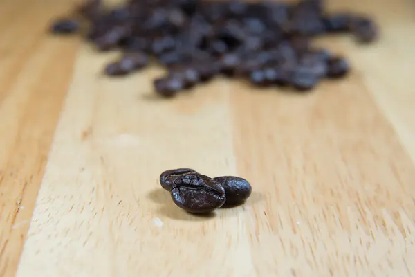 Kaffebönor och skugga på trä bakgrund, selektiv inriktning — Stockfoto