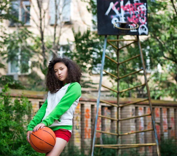 Retrato de una joven morena con una pelota de baloncesto en la calle — Foto de Stock