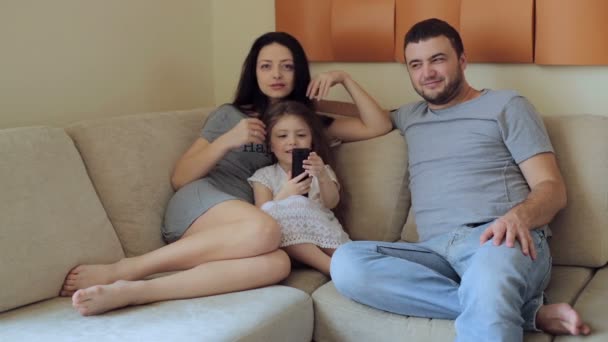 Junge Familie sitzt auf dem Sofa vor dem Fernseher — Stockvideo