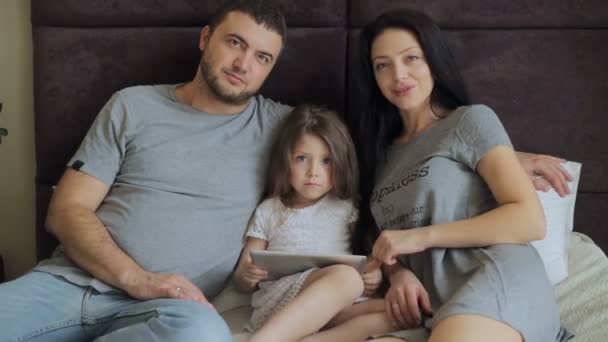Familia feliz acostada en la cama y mirando la Tabla — Vídeo de stock