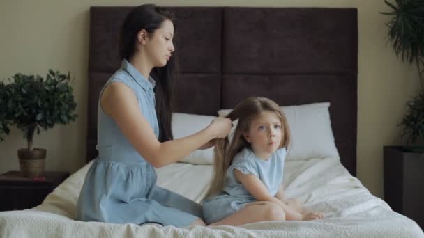 Madre pettinando i capelli della figlia sul letto a casa — Video Stock