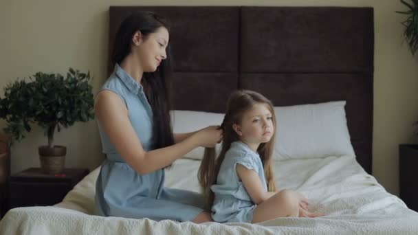 Madre peinando el pelo hija en la cama en casa — Vídeo de stock