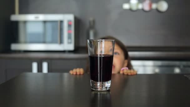 Маленькая девочка берет стакан сока и пьет — стоковое видео