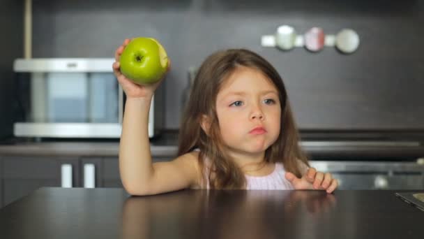 Маленька дівчинка їсть зелене яблуко і посміхається — стокове відео
