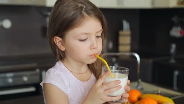 Little girl drinking milk through a straw from a glass — Stock Video