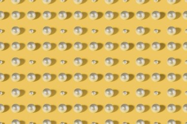 Sarı pastel arka planda gümüş renkli parlak Noel süsleri. Noel süsleri. Soyut minimal bileşim kusursuz model arkaplanı. Noel ve Yeni Yıl konsepti. Üst manzara, düz uzanma