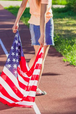 Ellerinde Amerika Birleşik Devletleri bayrağı olan bir kadın, açık havada, yumuşak odaklı arka planda