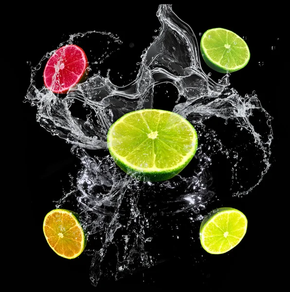 Żółte owoce cytrusowe (limonka, grejpfrut, cytryna) na czarnym tle z plusk wody — Zdjęcie stockowe