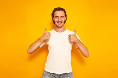 Yakışıklı Asyalı adam gülümsüyor ve gri arka planda baş parmak işareti yapıyor.