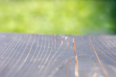 Bulanık yeşil arkaplanı olan ahşap bir yüzeye yakın plan. Tahtanın görünür tahıl desenleri ve doğal bir bitişi var.